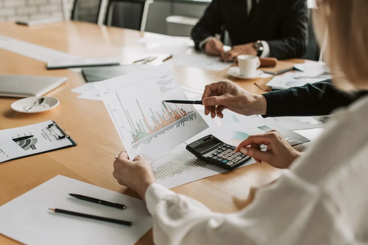 Two finance professionals reviewing bar-chart revenue reports and calculating figures at a conference table